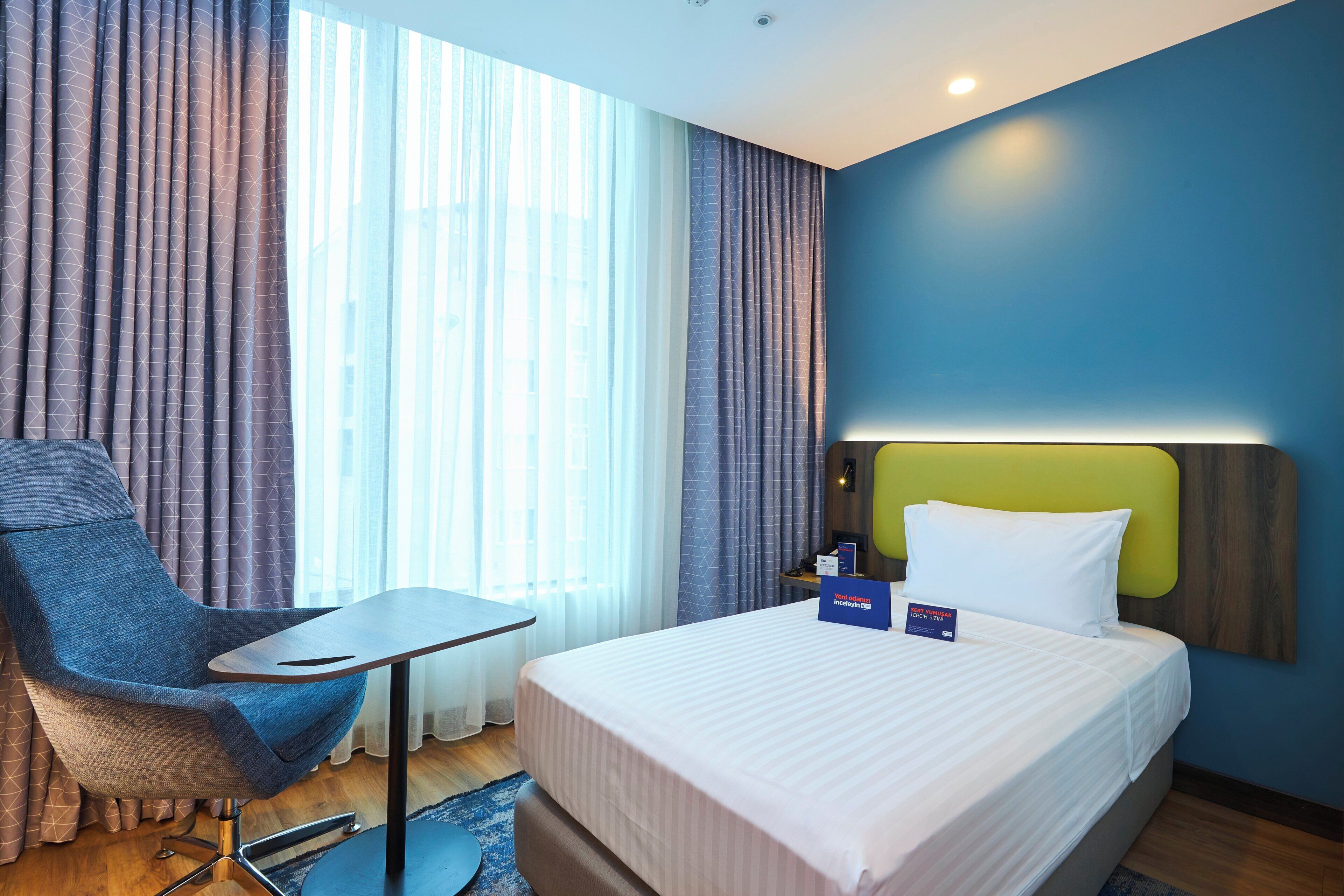A hotel room with a bed, a chair, a table, and a nightstand.