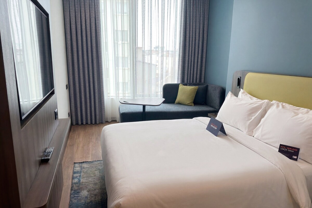 A hotel room with a bed, a small table, a sofa, and a TV.