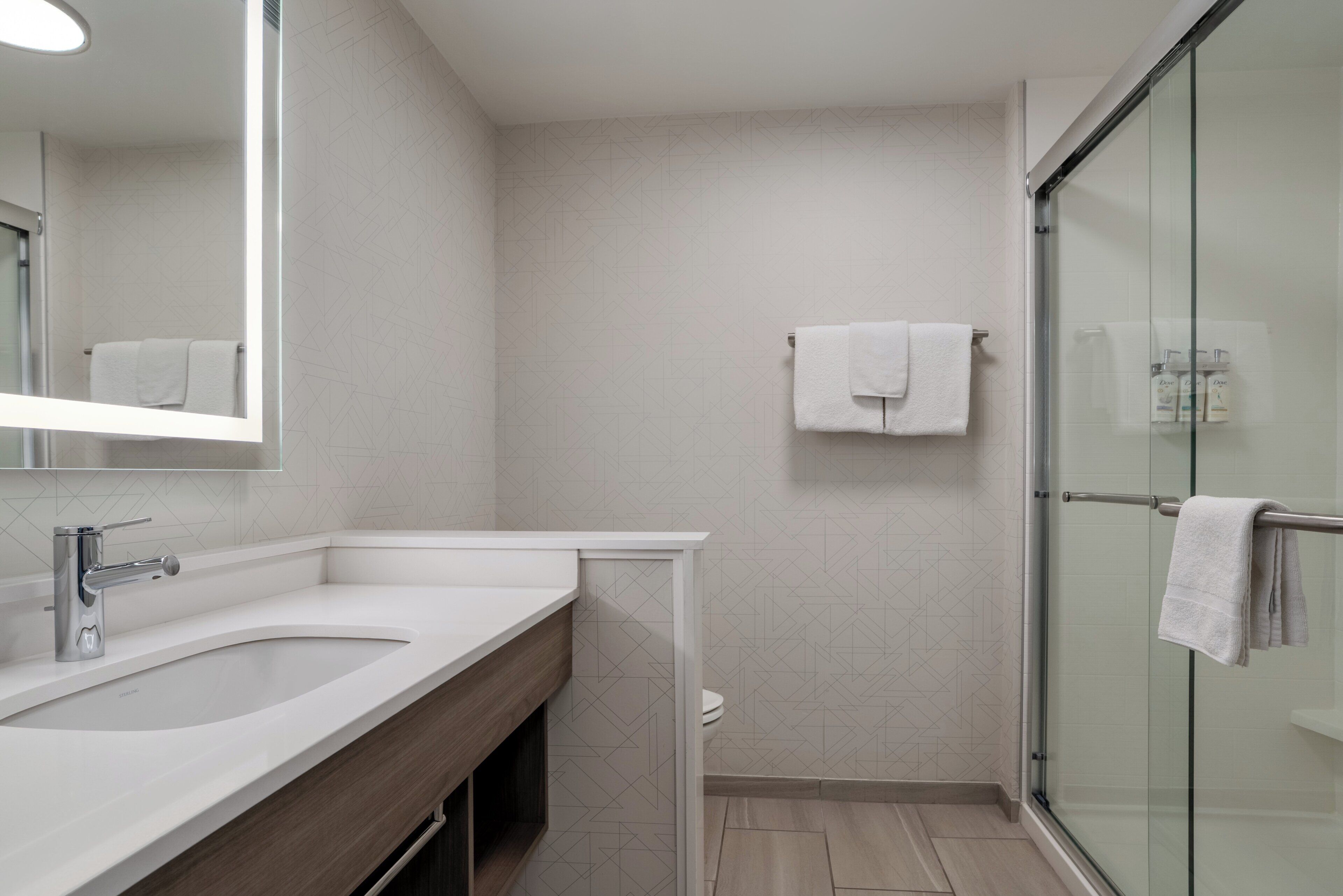 Un baño moderno con un espejo grande, un lavamanos, un inodoro y una cabina de ducha de vidrio.