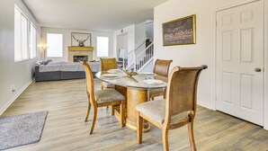 A dining area with a round table set for six, surrounded by wooden chairs with cushioned seats. A fireplace is visible in the background, and a staircase leads to an upper level. - Pool Table & Charcoal Grill: Home in Victorville! (Victorville)