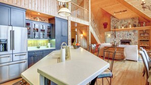 Een ruime keuken met een groot schiereiland, houten kastjes en een stenen openhaard.