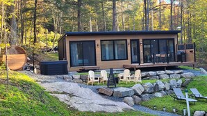 Una cabaña moderna con amplios ventanales, mobiliario exterior y una terraza.