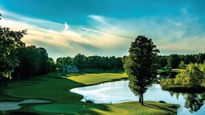 Un campo de golf con un estanque, árboles y cielo despejado.