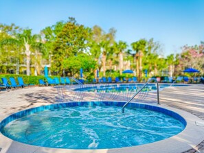 Un bain à remous bordé de carreaux, entouré de chaises longues et de parasols, avec des arbres et un ciel dégagé en arrière-plan.