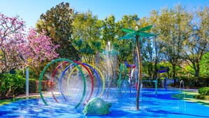 Un área de juegos acuáticos con una gran escultura de tortuga verde, aros de colores y una estructura de juego verde y azul.