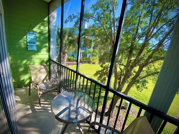 Un balcon avec une table en verre et deux chaises, donnant sur une pelouse verdoyante et des arbres.