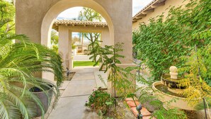 An outdoor courtyard with a fountain, potted plants, and a view of a house through an archway. - Family Friendly: Spacious Oasis in Palm Desert! (Palm Desert)