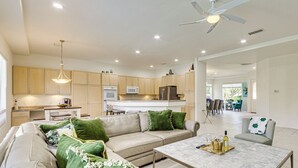 A modern kitchen with wooden cabinets, a dining area with a table and chairs, and a living room with a sofa and green cushions. - Family Friendly: Spacious Oasis in Palm Desert! (Palm Desert)