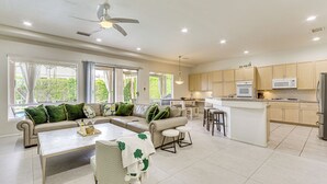 A spacious living area with a sofa, coffee table, and a dining table. A kitchen with a microwave and refrigerator is visible in the background. - Family Friendly: Spacious Oasis in Palm Desert! (Palm Desert)