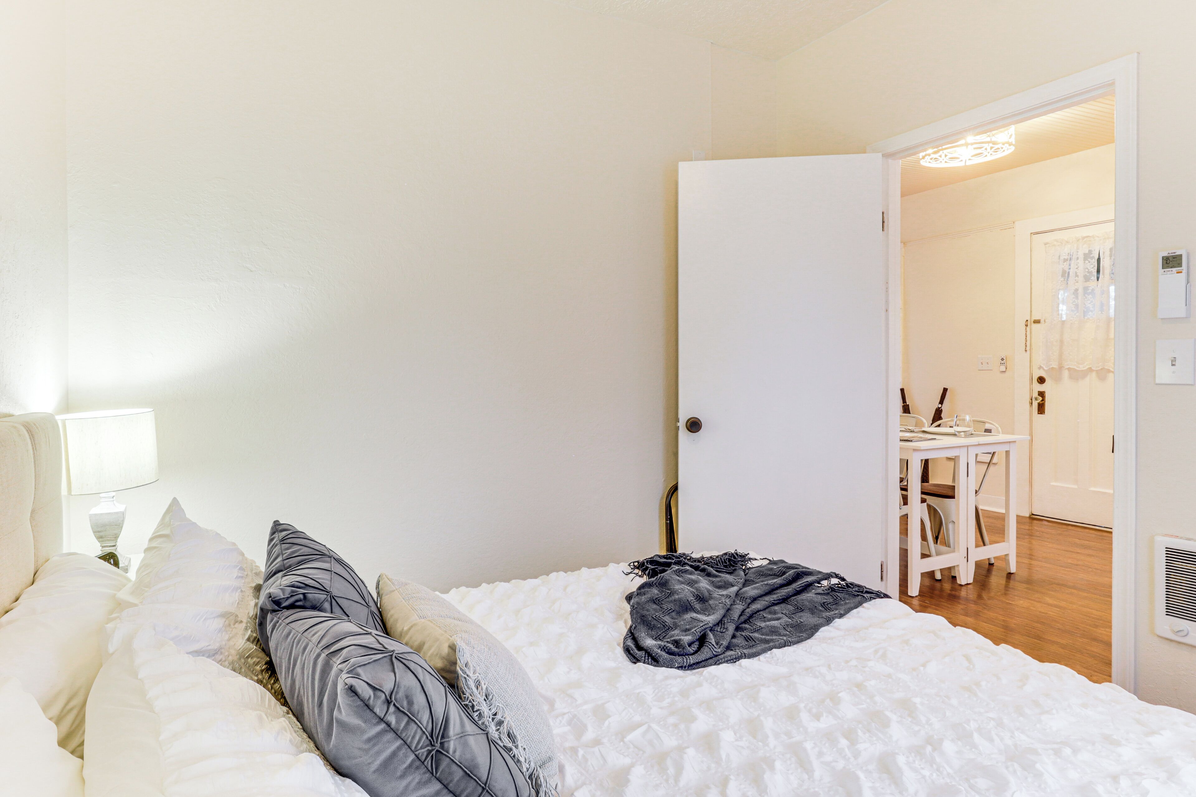 A bedroom with a bed, pillows, a bedside table with a lamp, and a door leading to a bathroom.