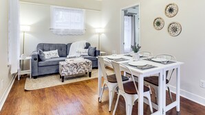 A living room with a grey sofa, a small table, and a dining area with white chairs. - Walkable Location: Quaint Cottage in Forest Grove! (Forest Grove)