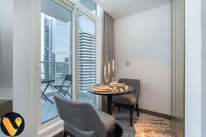 A modern hotel room with a balcony, a round dining table set with candles, and a view of city buildings.