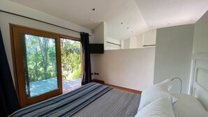 Une chambre dotée d’un grand lit, d’un téléviseur fixé au mur et d’une porte-fenêtre coulissante donnant sur un balcon.