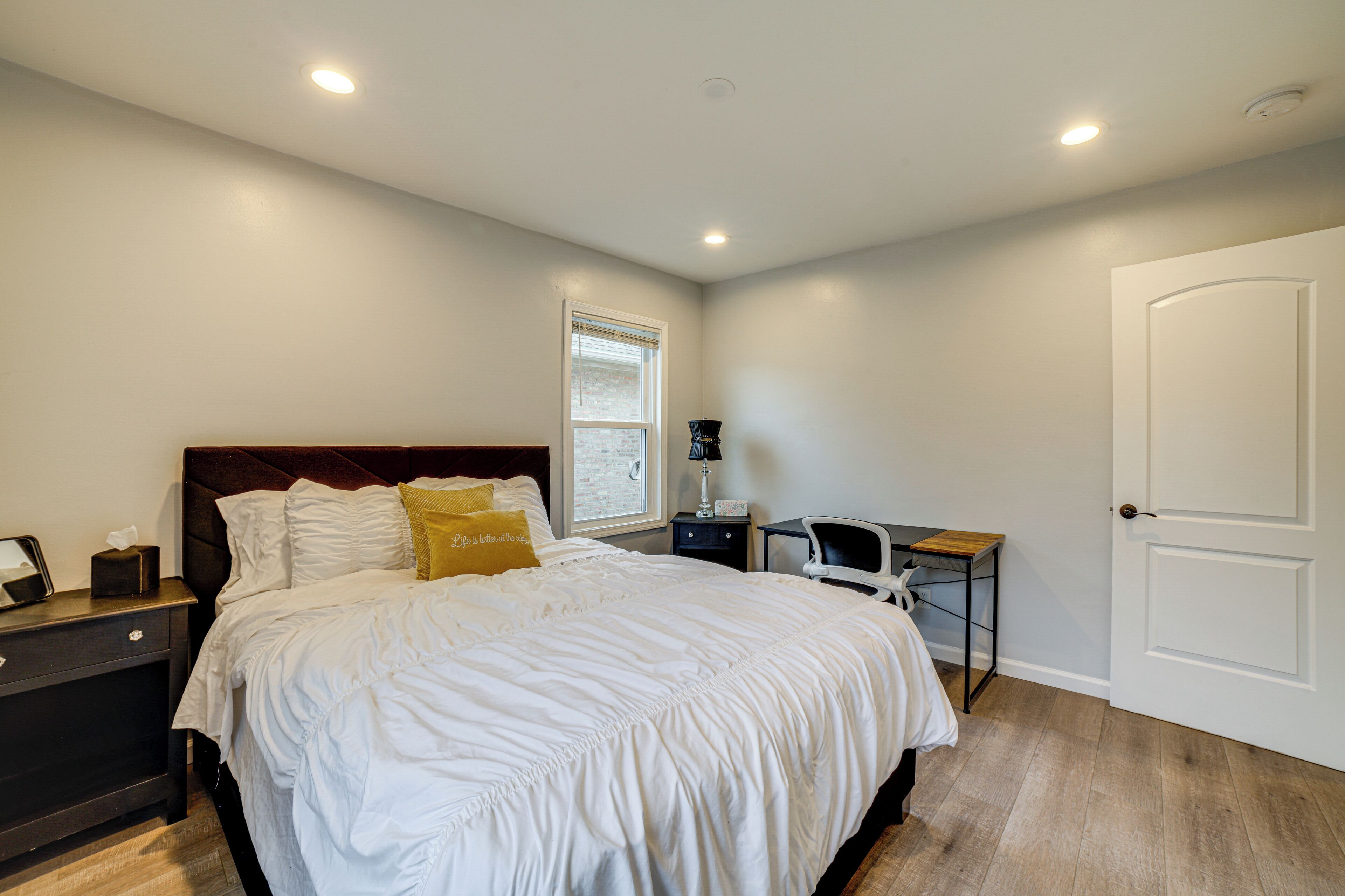 A bedroom with a large bed, a nightstand, a desk, and a door.
