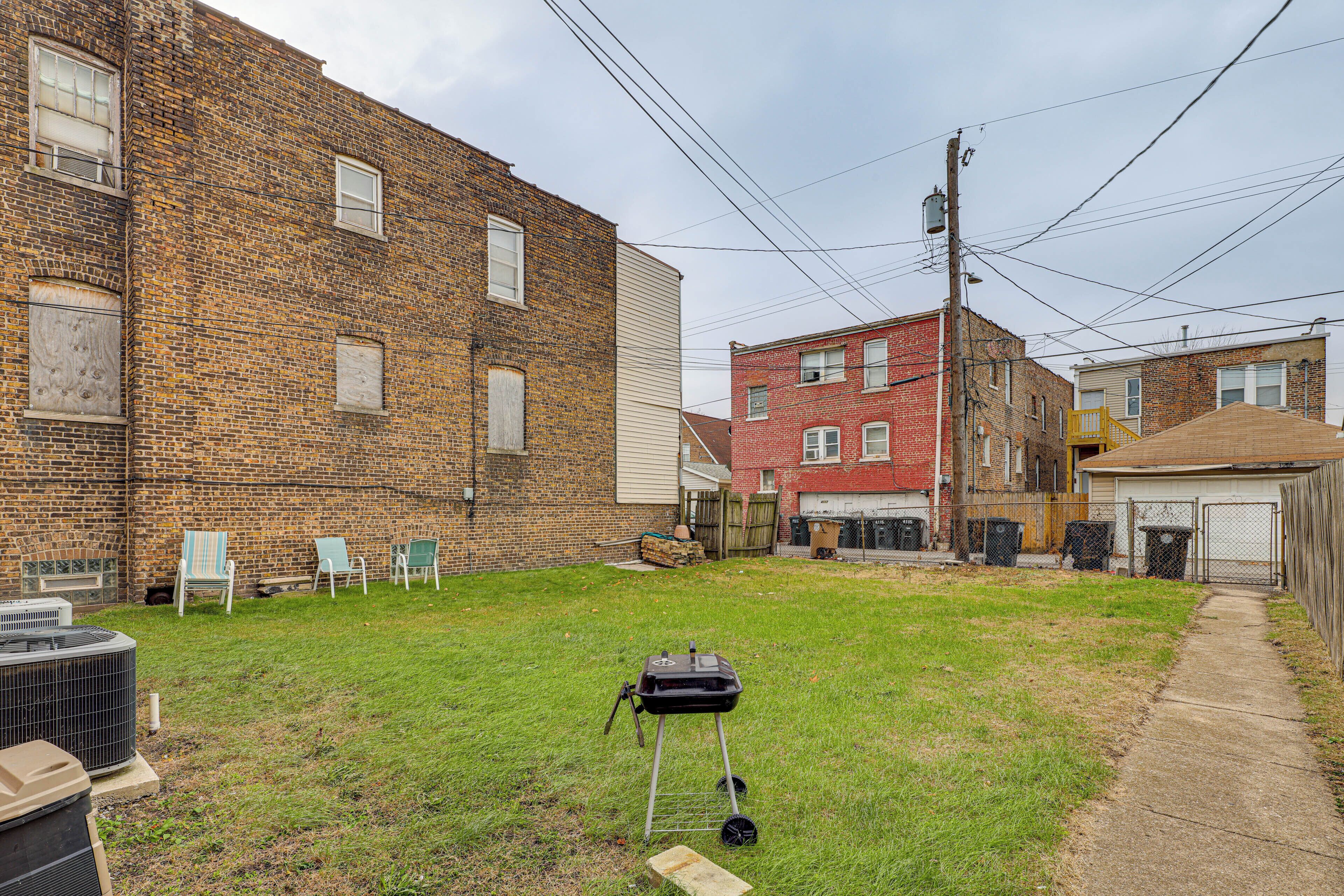 A backyard with a grill, chairs, and a brick building.