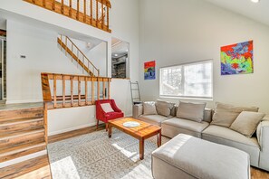 A spacious living area with a wooden staircase, a red armchair, a beige sofa, and a coffee table.