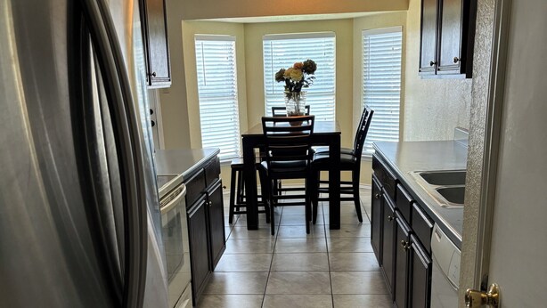 A kitchen with a stainless steel refrigerator, a dining table with chairs, and a vase with flowers.