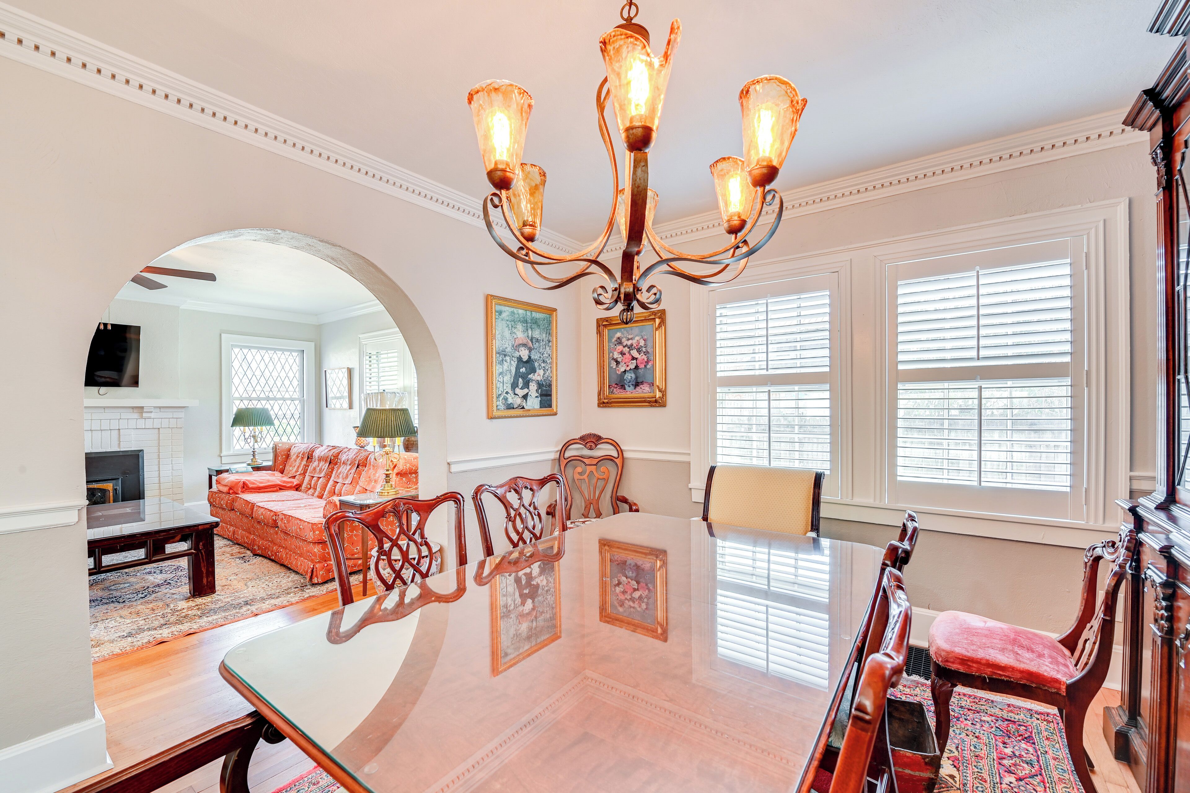 Uma sala de estar ampla com uma grande mesa de jantar, cadeiras de madeira elegante, um candelabro e uma lareira.