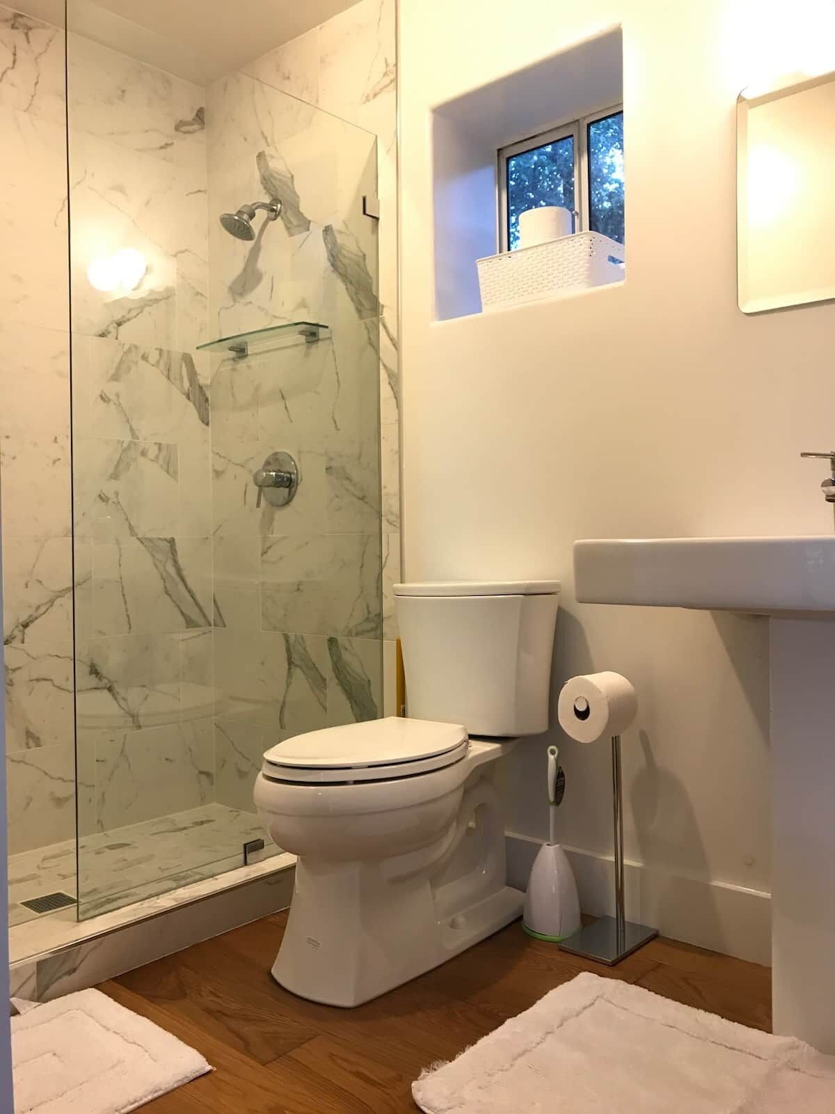 A bathroom with a glass-enclosed shower, a toilet, and a sink.