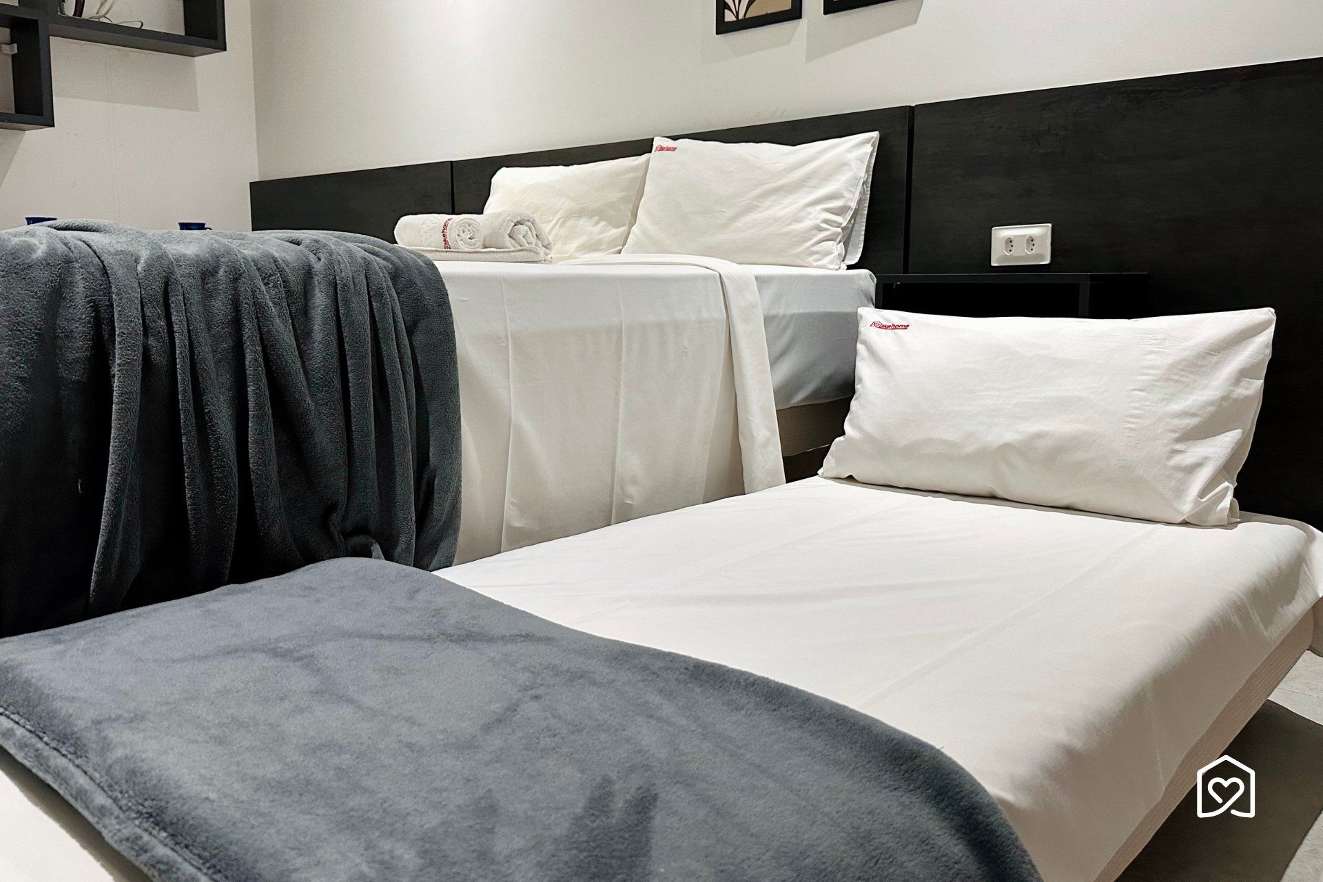 Une chambre d’hôtel avec deux lits, l’un recouvert d’une couverture grise et l’autre de draps blancs.