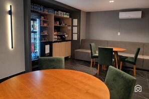 Un interior moderno con una mesa redonda de madera, sillas tapizadas en verde, un sofá y un refrigerador con bebidas.