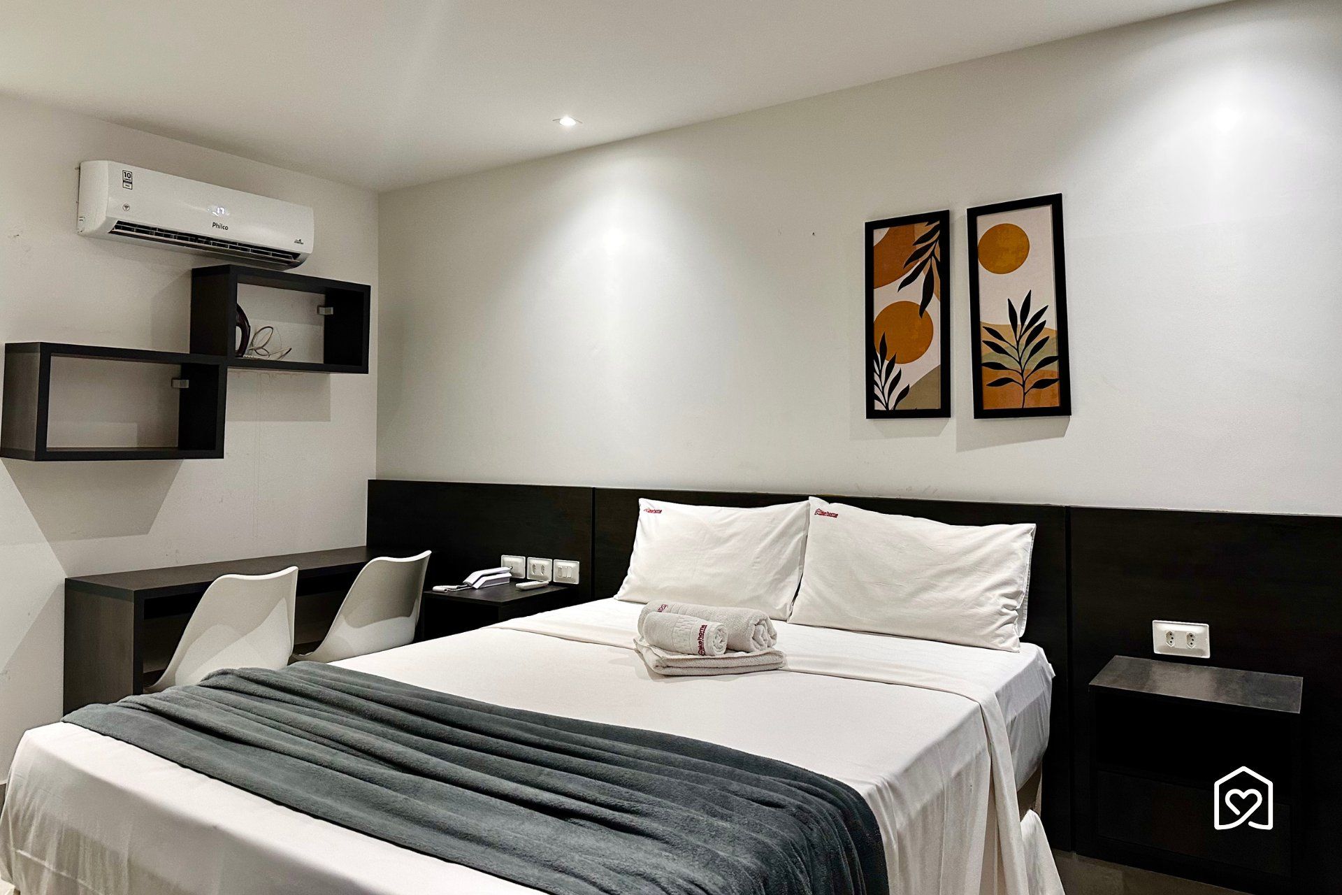 Une chambre d’hôtel comprenant un lit, des tables de chevet, un bureau, une chaise, un appareil de climatisation et des œuvres d’art accrochées au mur.
