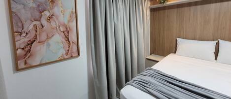 A modern hotel room with a large bed, grey curtains, a wooden headboard, and a marble artwork on the wall.