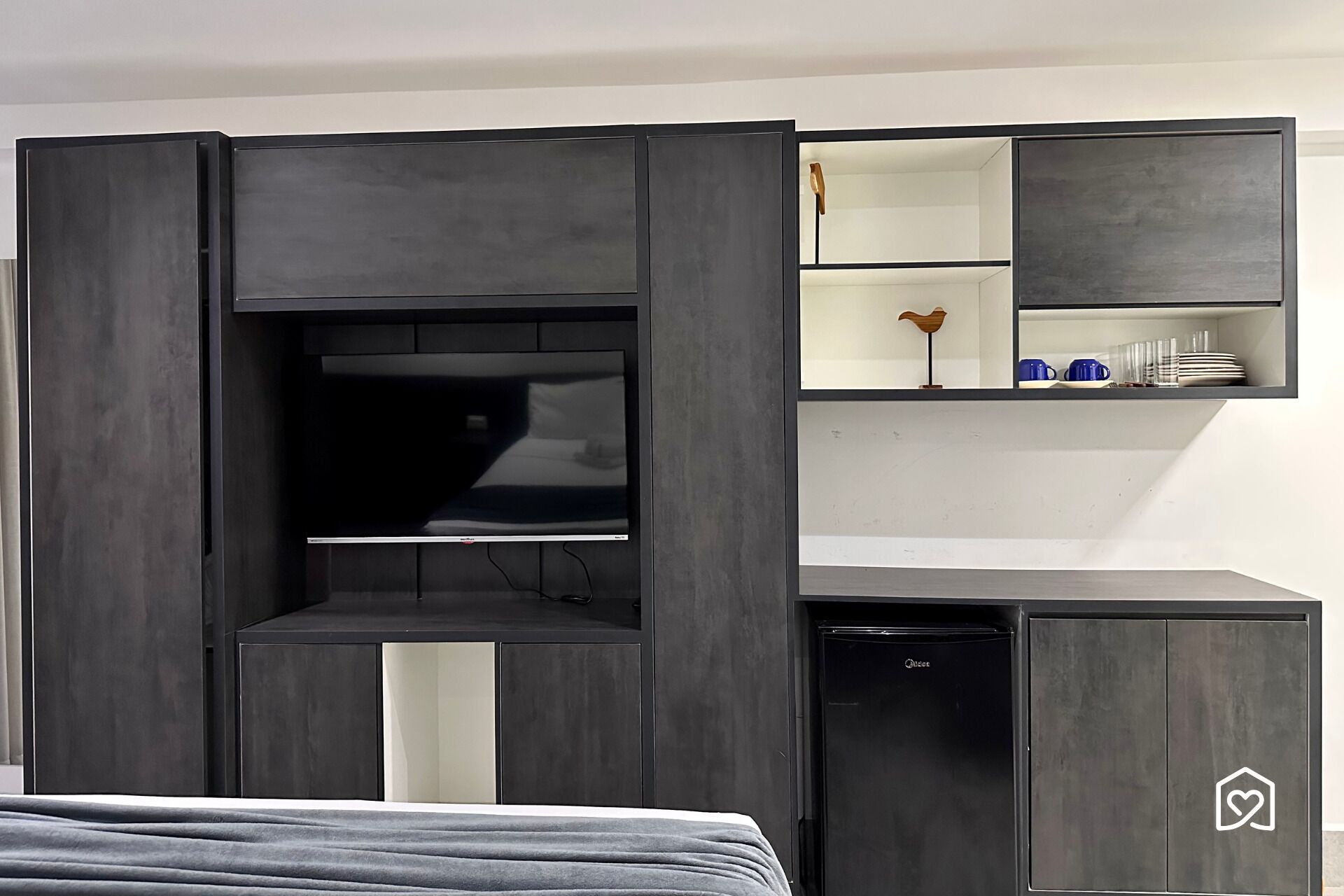 A room with a bed, a TV, a small shelf with items, and a cabinet.