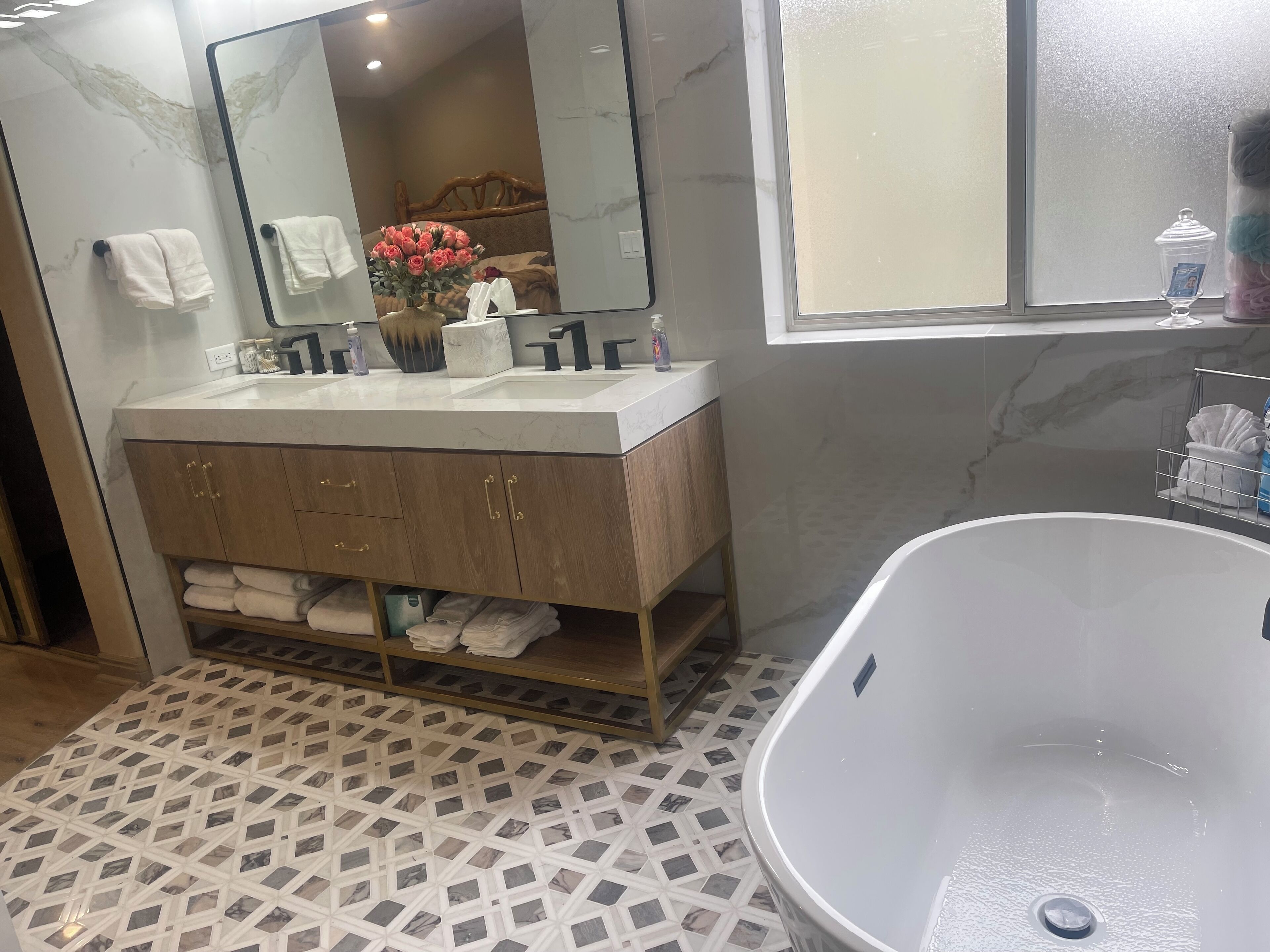 Un baño con suelo de mármol, un espejo grande, un tocador de madera con lavabo y una bañera.