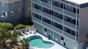 Un edificio de varios pisos con piscina en la azotea, balcones y un patio amurallado.