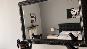 Ein Schlafzimmer mit Bett, Nachttisch, Lampe und einem Spiegel, der den Raum reflektiert.