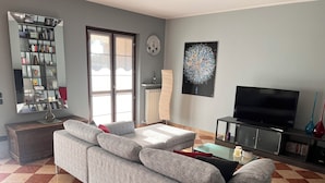 Ein Wohnzimmer mit grauem Sofa, einem Fernseher und einem Bücherregal.