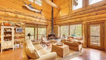L’intérieur d’une cabane en rondins, avec une cheminée, des meubles en bois et de grandes fenêtres.