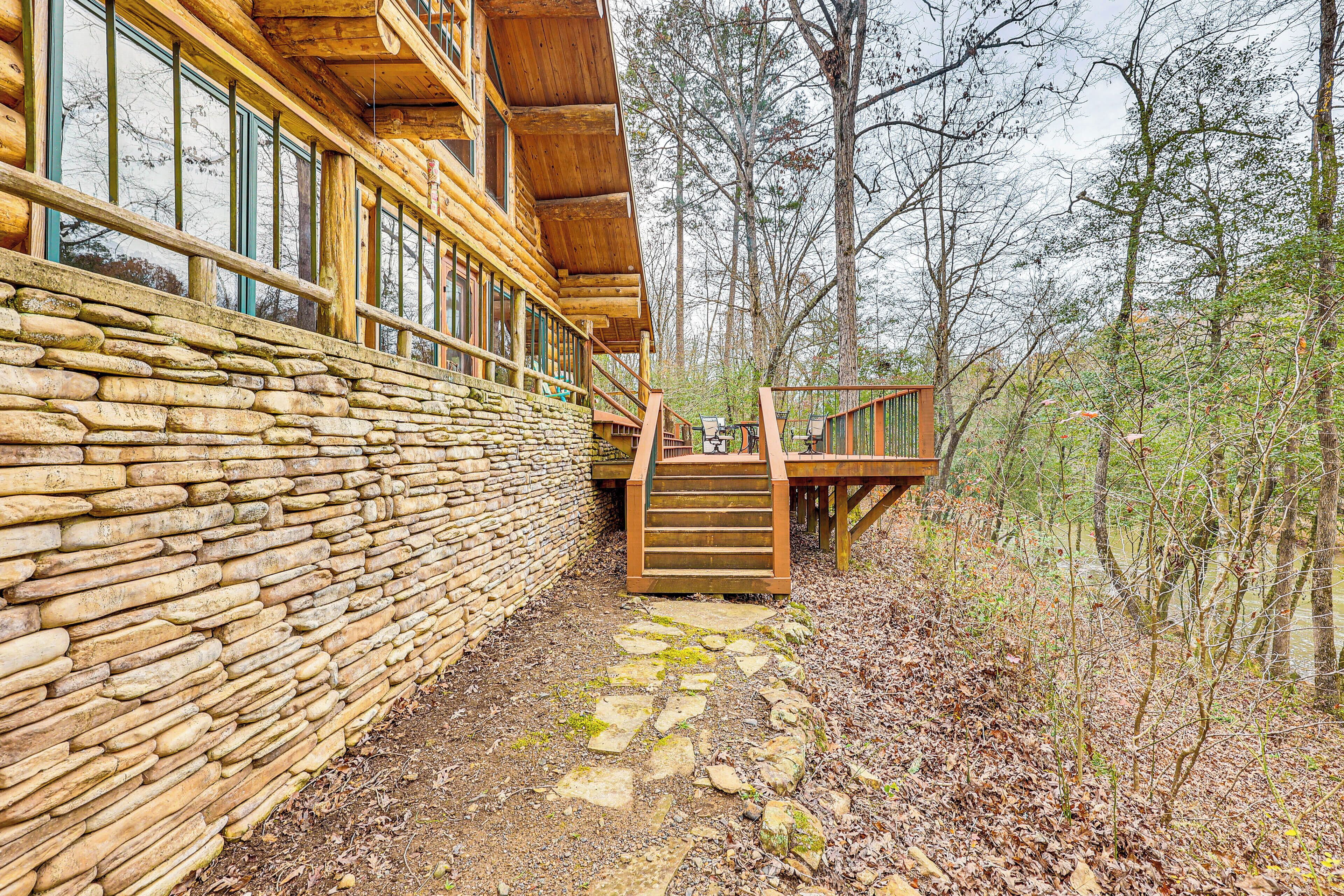Une cabane en rondins avec un mur en pierre, une terrasse en bois et un escalier menant à un porche.