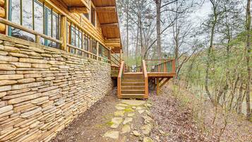 Une cabane en rondins avec un mur en pierre, une terrasse en bois et un escalier menant à un porche.