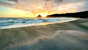 Una playa con atardecer, olas y una montaña distante.