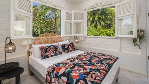Un dormitorio con cama, paredes blancas y ventanas con contraventanas.