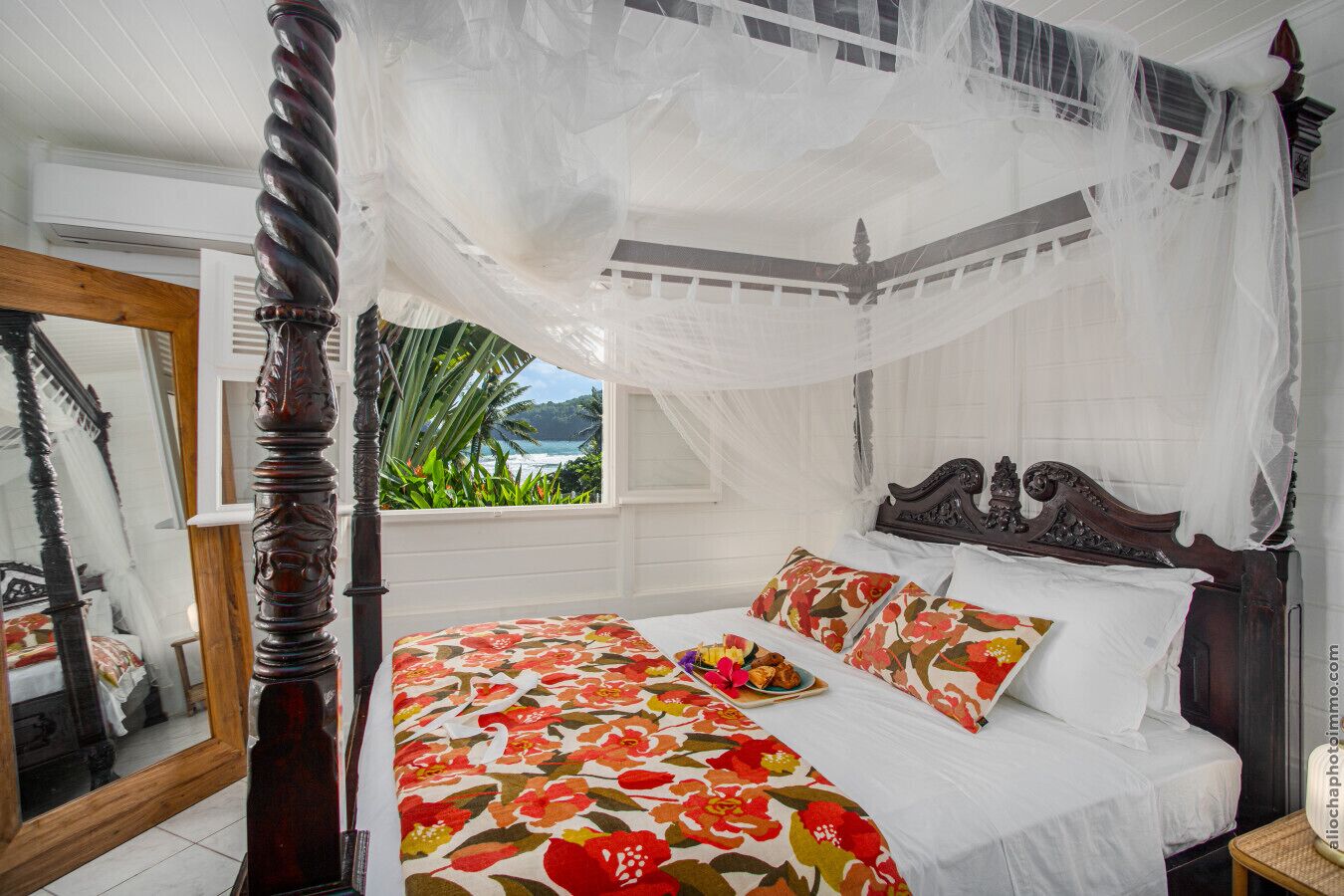 Una cama con dosel, cubrecama floral y almohadas.