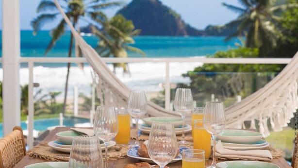 Une table dressée pour le petit-déjeuner, avec vue sur l’océan et les palmiers.