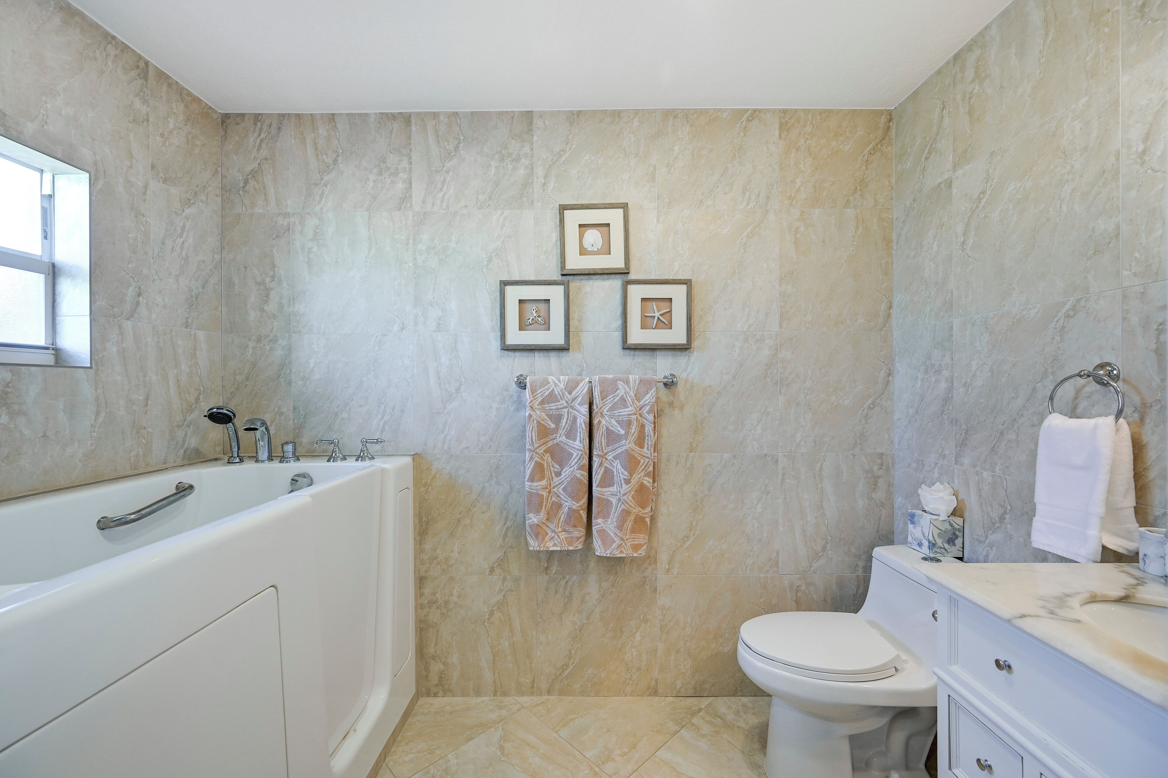 A bathroom with a bathtub, toilet, and vanity. There are three framed pictures on the wall.