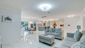 A modern living room with a grey sofa, ottoman, and a dining area with a table and chairs. - Pool & Spa: Luxe Home in Naples! (Naples)