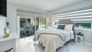 A bedroom with a large bed, a nightstand, a lamp, and a view of the outdoors. - Pool & Spa: Luxe Home in Naples! (Naples)