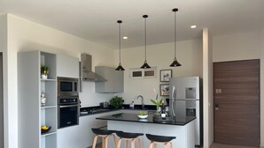 Una cocina moderna con una isla central, taburetes de bar, electrodomésticos de acero inoxidable e iluminación colgante.