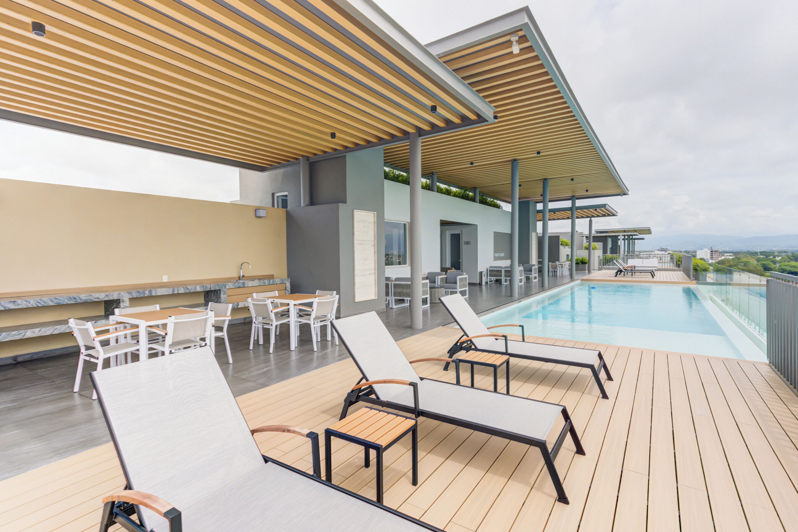 A rooftop pool area with lounge chairs and tables, a clear view of the cityscape, and a modern architectural design.