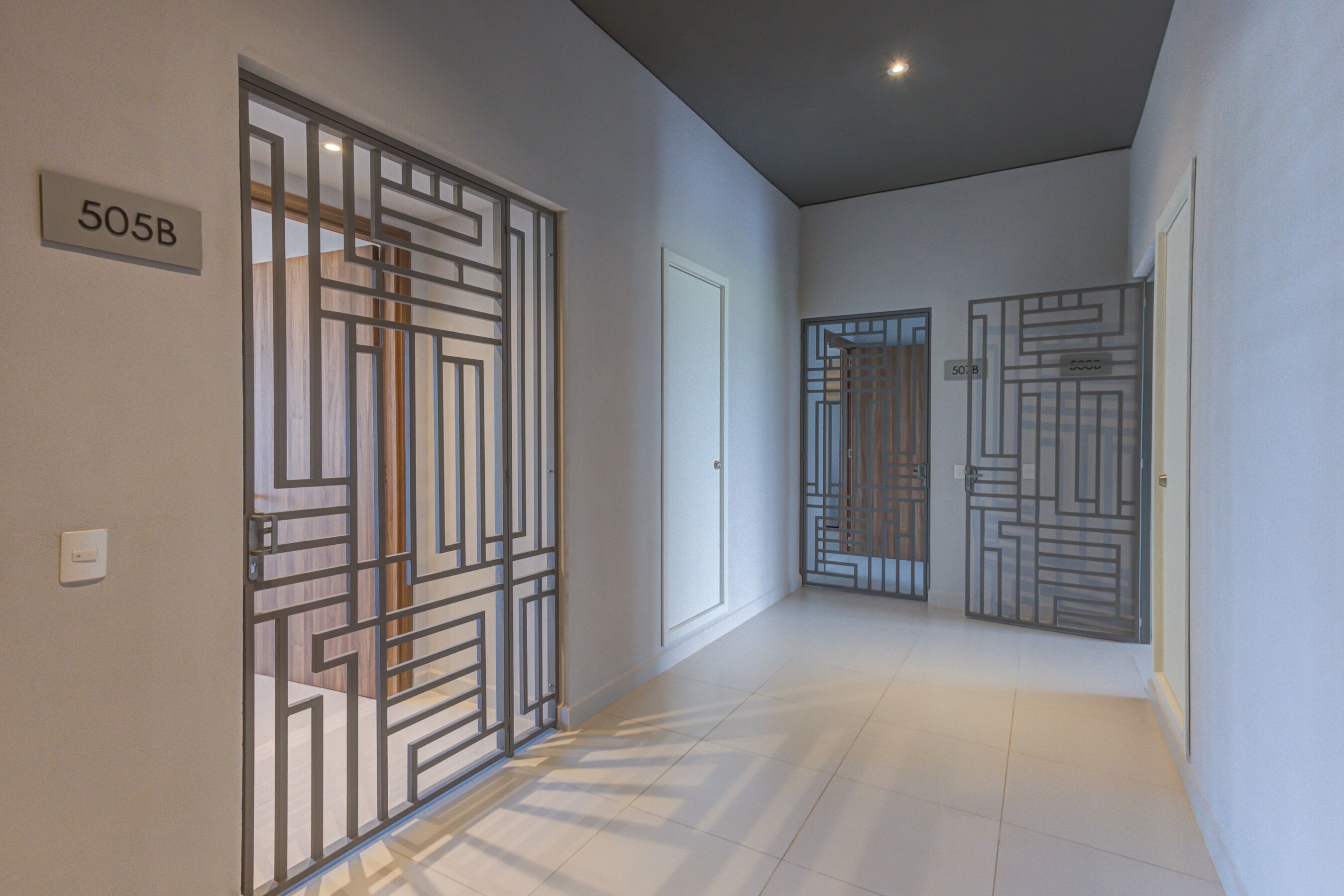A hallway with three doors, each with a geometric metal gate design. A sign on the wall reads "505B".