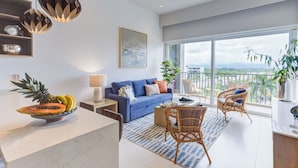 A modern living room with a blue sofa, a dining area with a white table, and a balcony with wicker chairs. - Punto Novo Nuevo Vallarta Condos (Nuevo Nayarit)