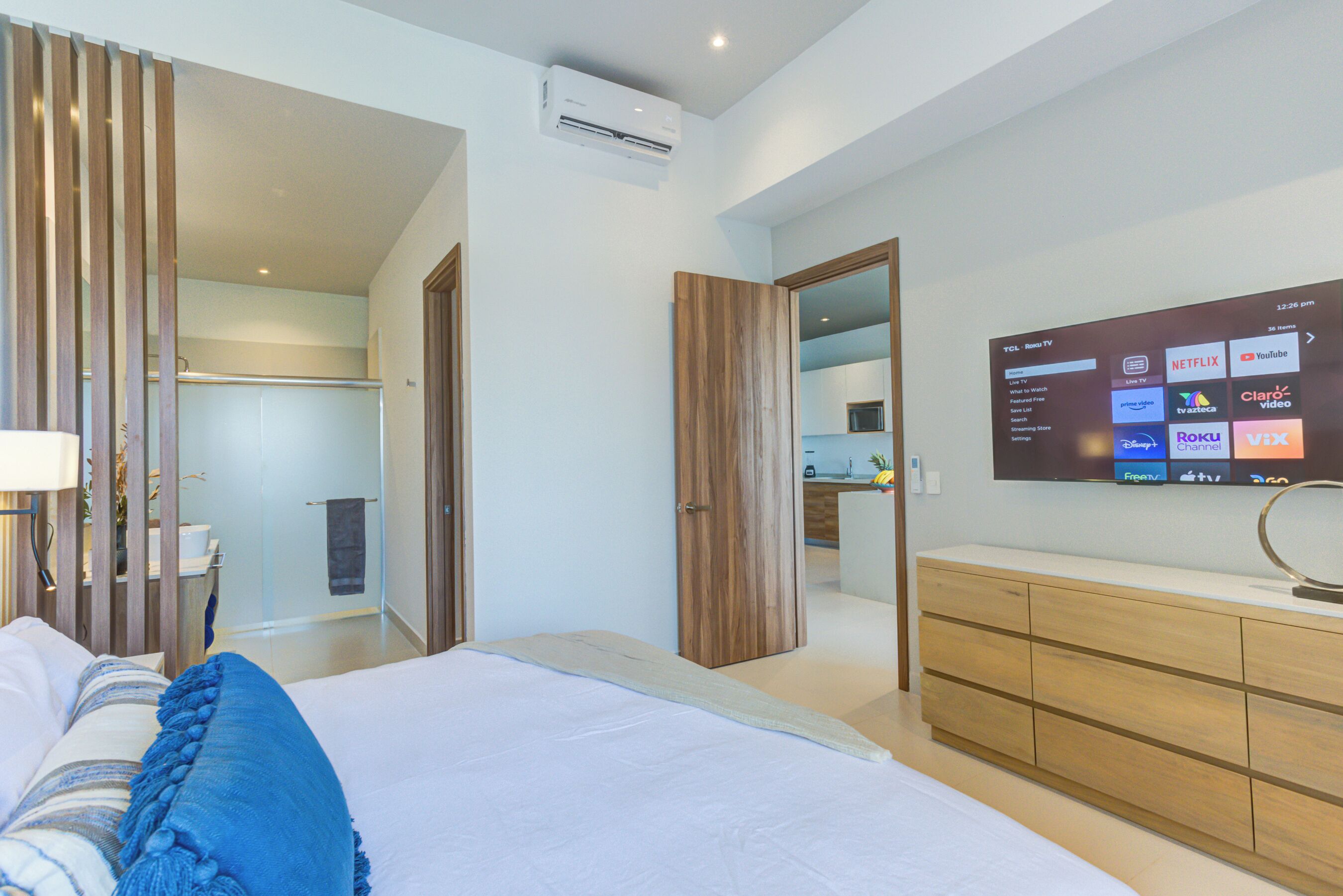 Une chambre d’hôtel moderne avec un grand lit, une commode en bois et un téléviseur fixé au mur permettant d’accéder à des services de diffusion en continu.
