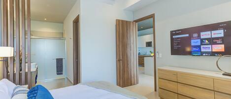 Une chambre d’hôtel moderne avec un grand lit, une commode en bois et un téléviseur fixé au mur permettant d’accéder à des services de diffusion en continu.