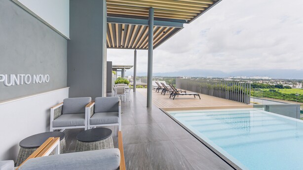 A rooftop pool area with lounge chairs, a wooden deck, and a view of the cityscape. - Punto Novo Nuevo Vallarta Condos (Nuevo Nayarit)