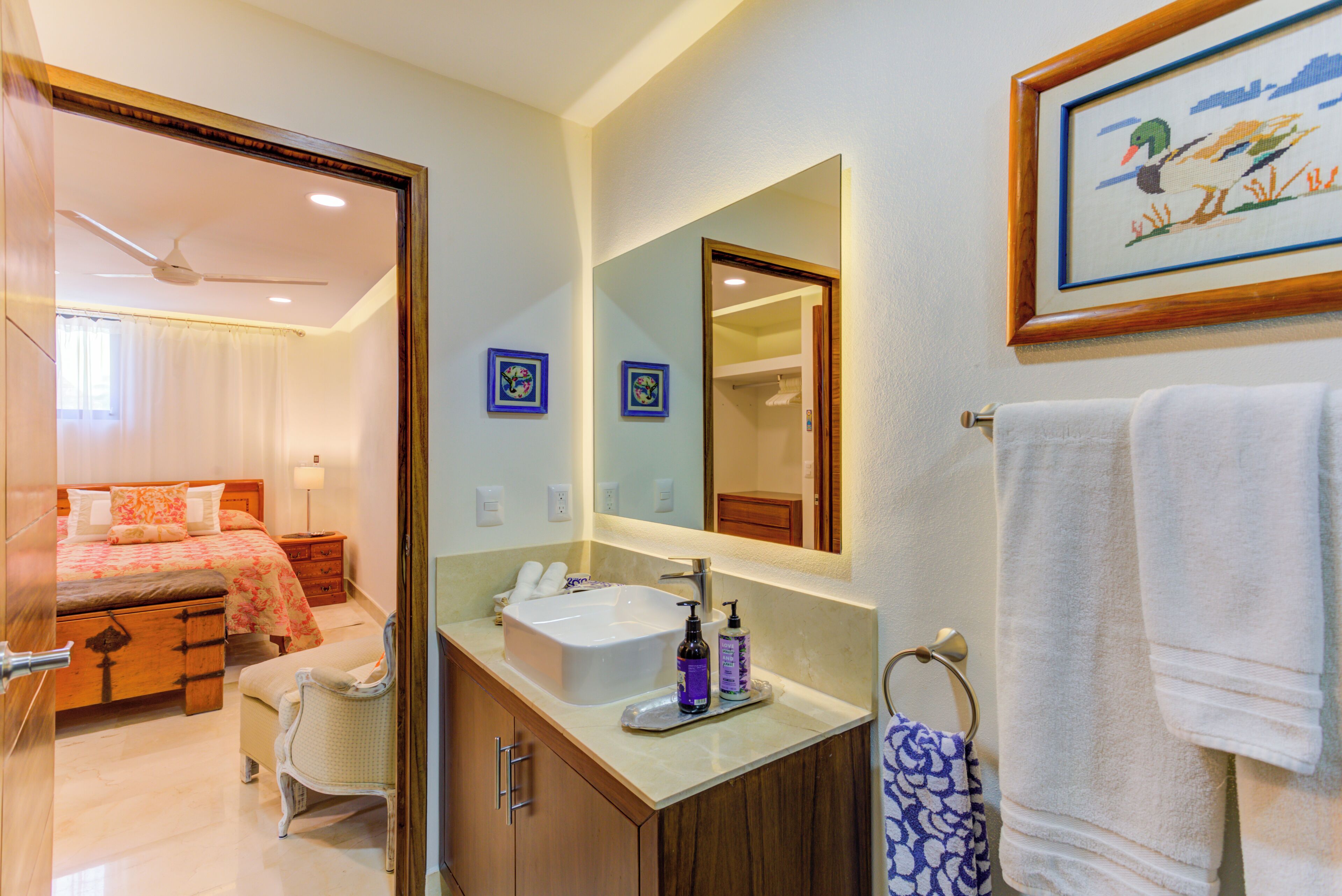 A hotel room with a bed, a bathroom with a sink and mirror, and a framed picture on the wall.